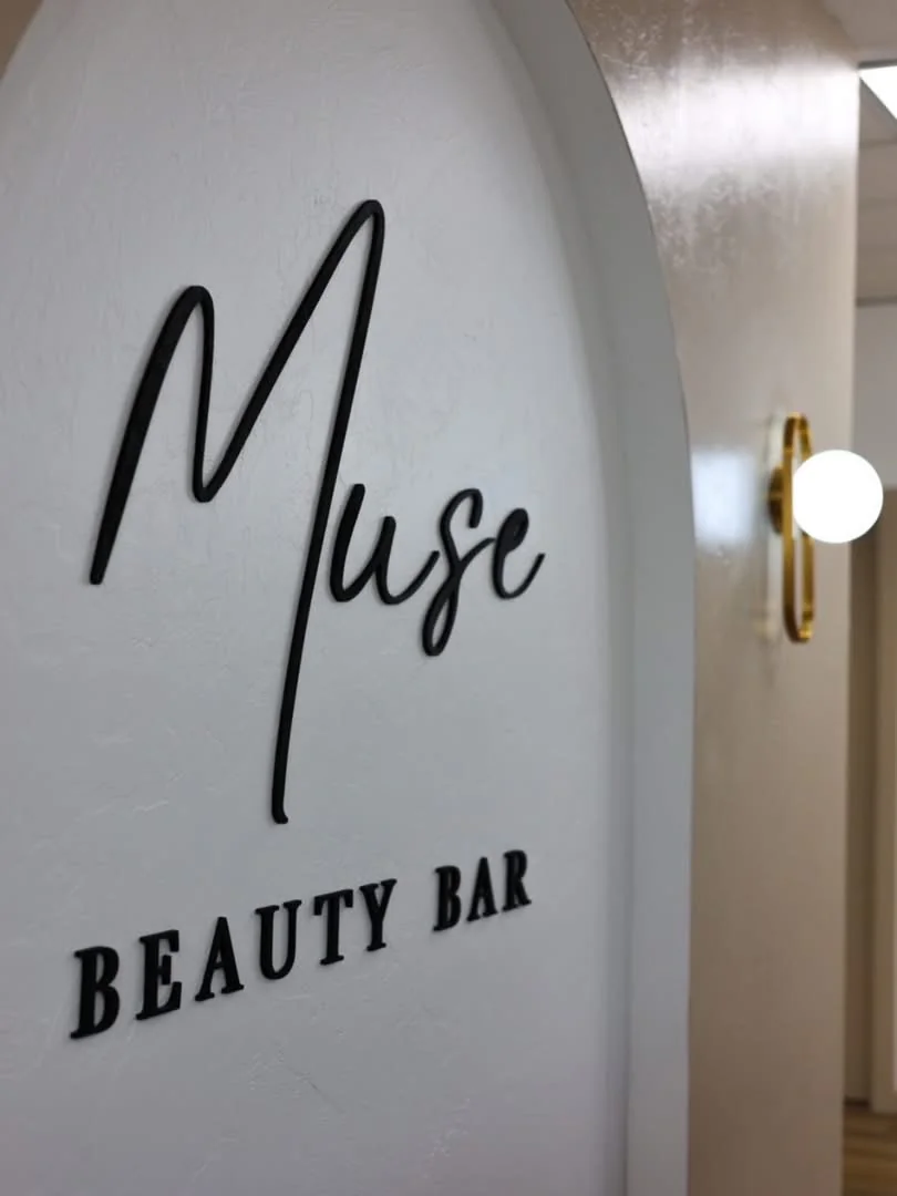 The Muse Beauty Bar arched logo wall and brushed-gold sconce