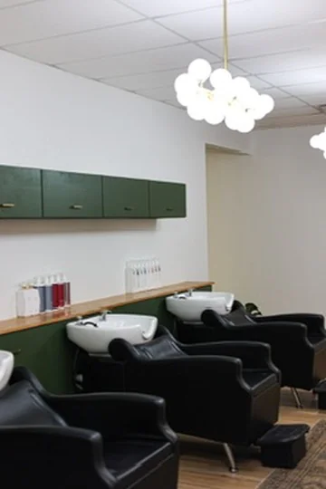 Muse shampoo lounge with black chairs, white basins, and globe pendant lights